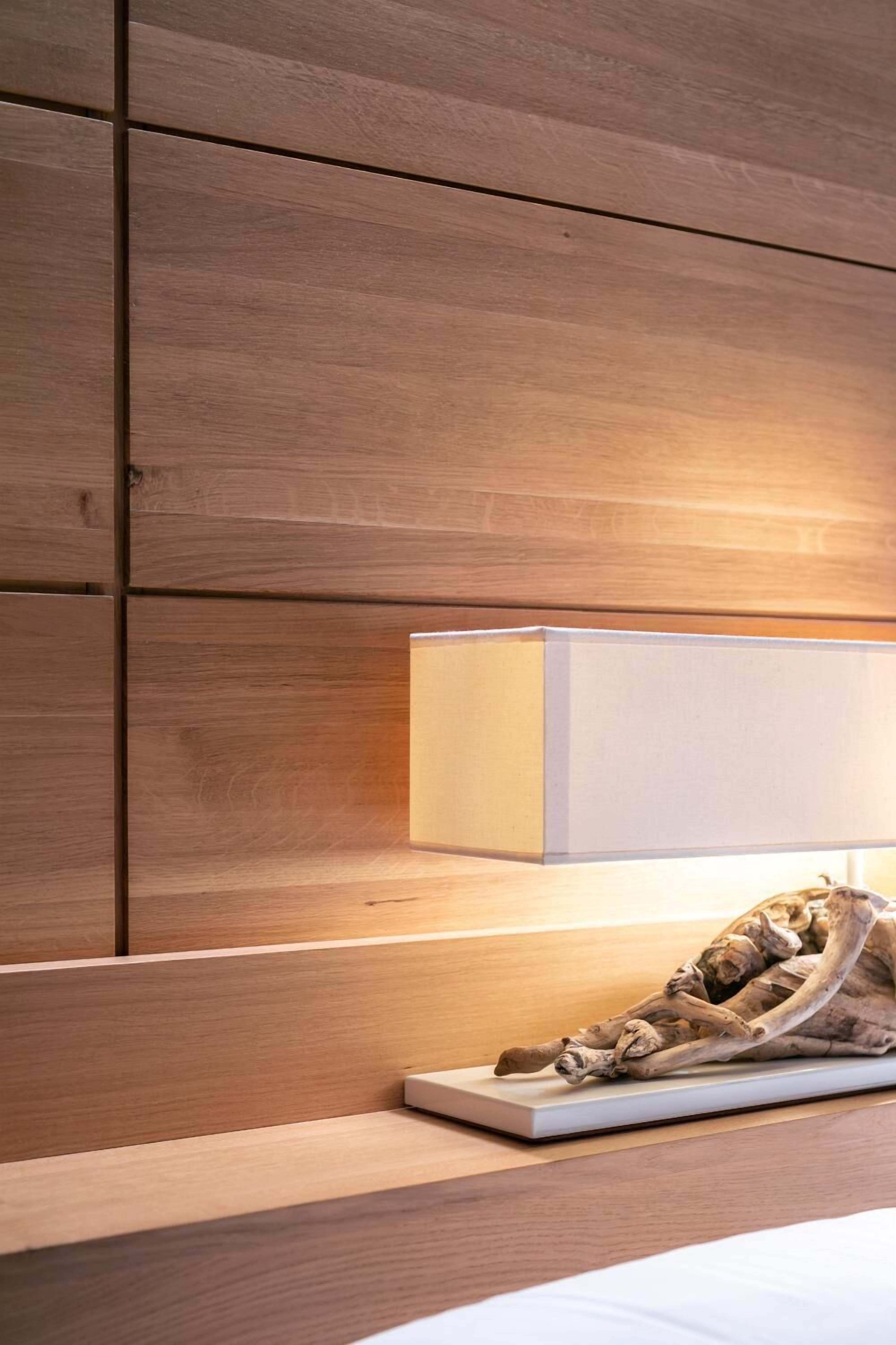 A wooden wall with a bedside lamp and a decorative piece on a nightstand.