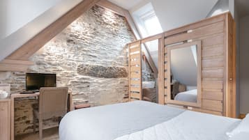 Een slaapkamer met een schuine plafond, stenen muur, houten bed en een bureau met stoel.