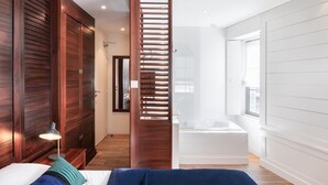 A modern bedroom with a large bed, a nightstand, a lamp, and a view of a bathroom with a bathtub. - La Vinotière (Le Conquet)