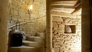 A stone staircase with a suitcase on the steps, a wall-mounted light, and a stone shelf with a decorative object. - La Vinotière (Le Conquet)