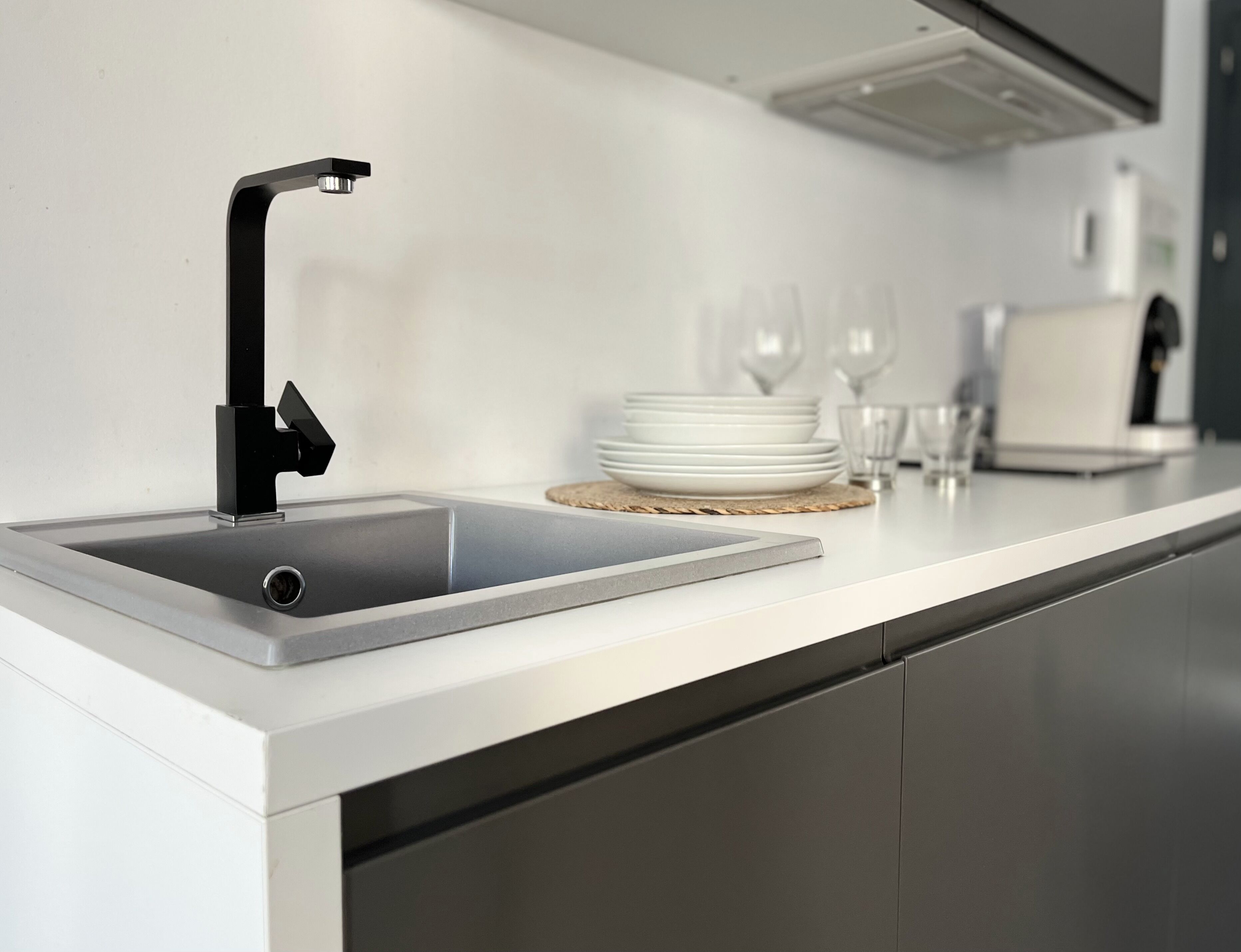 Una cocina moderna con un grifo negro elegante, un lavamanos de acero inoxidable y una encimera blanca.