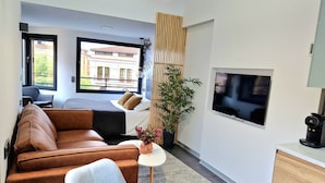 Een moderne hotelkamer met een bank, een bed, een klein tafeltje met een vaas, een potplant, een televisie en een koffiezetapparaat.