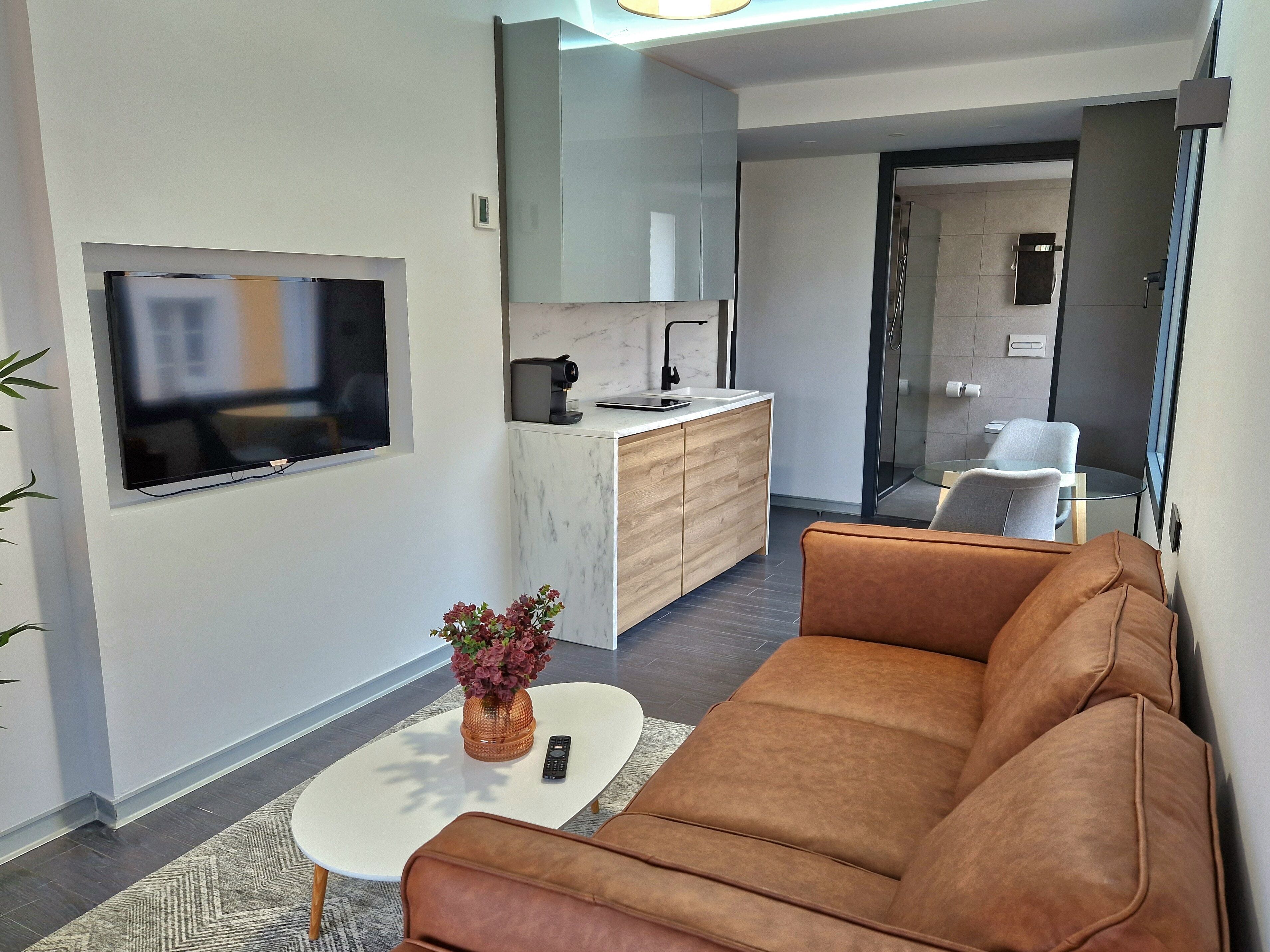 Ein modernes Wohnzimmer mit einem braunen Ledersofa, einem Couchtisch mit einer Vase und einem an der Wand montierten Fernseher.