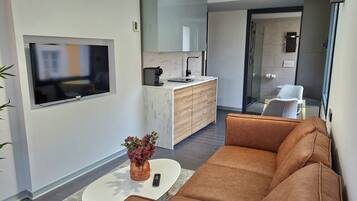 Una sala de estar moderna con un sofá de cuero marrón, una mesa de centro con un florero y un televisor montado en la pared.