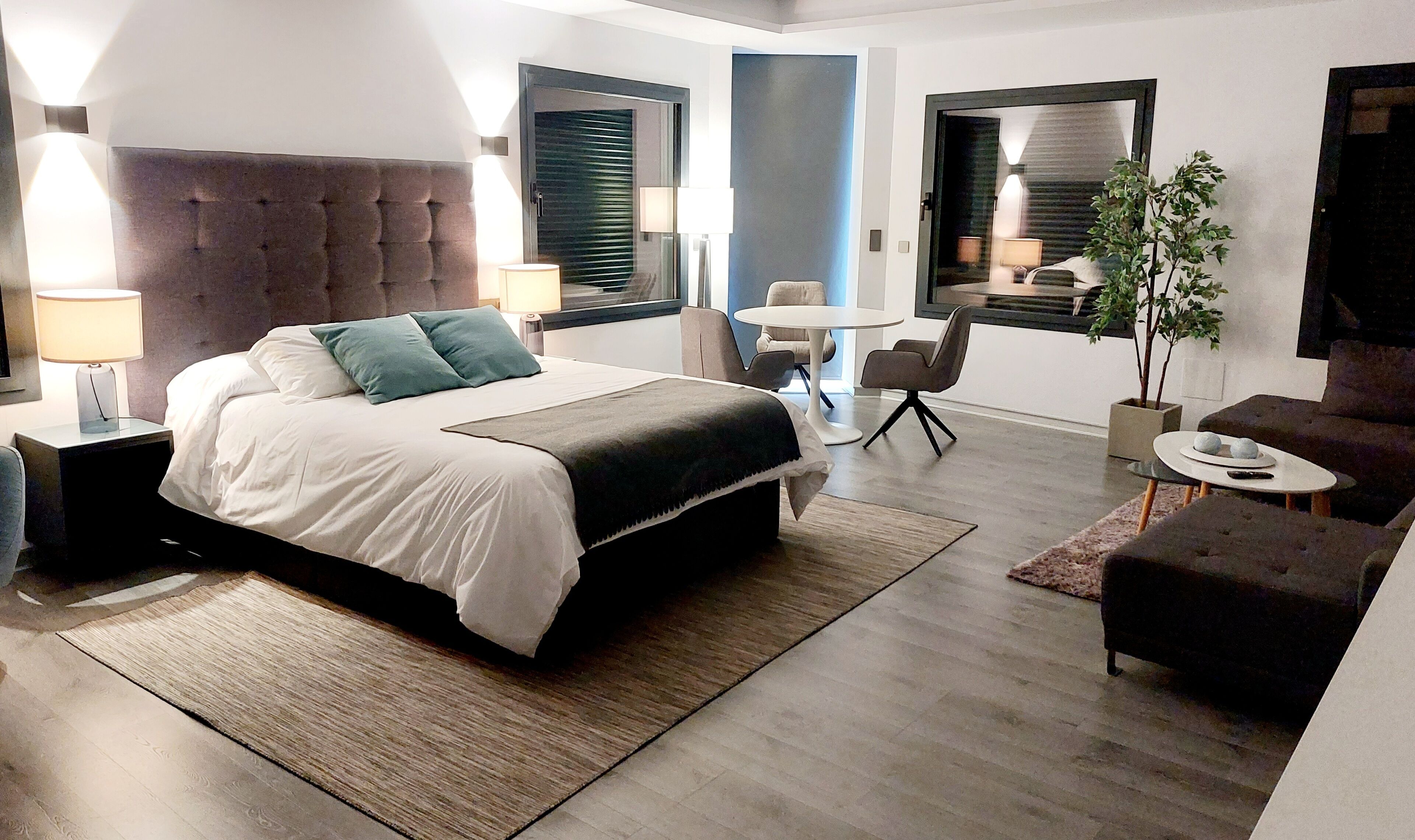 A modern hotel room with a large bed, a desk, a chair, and a sofa.