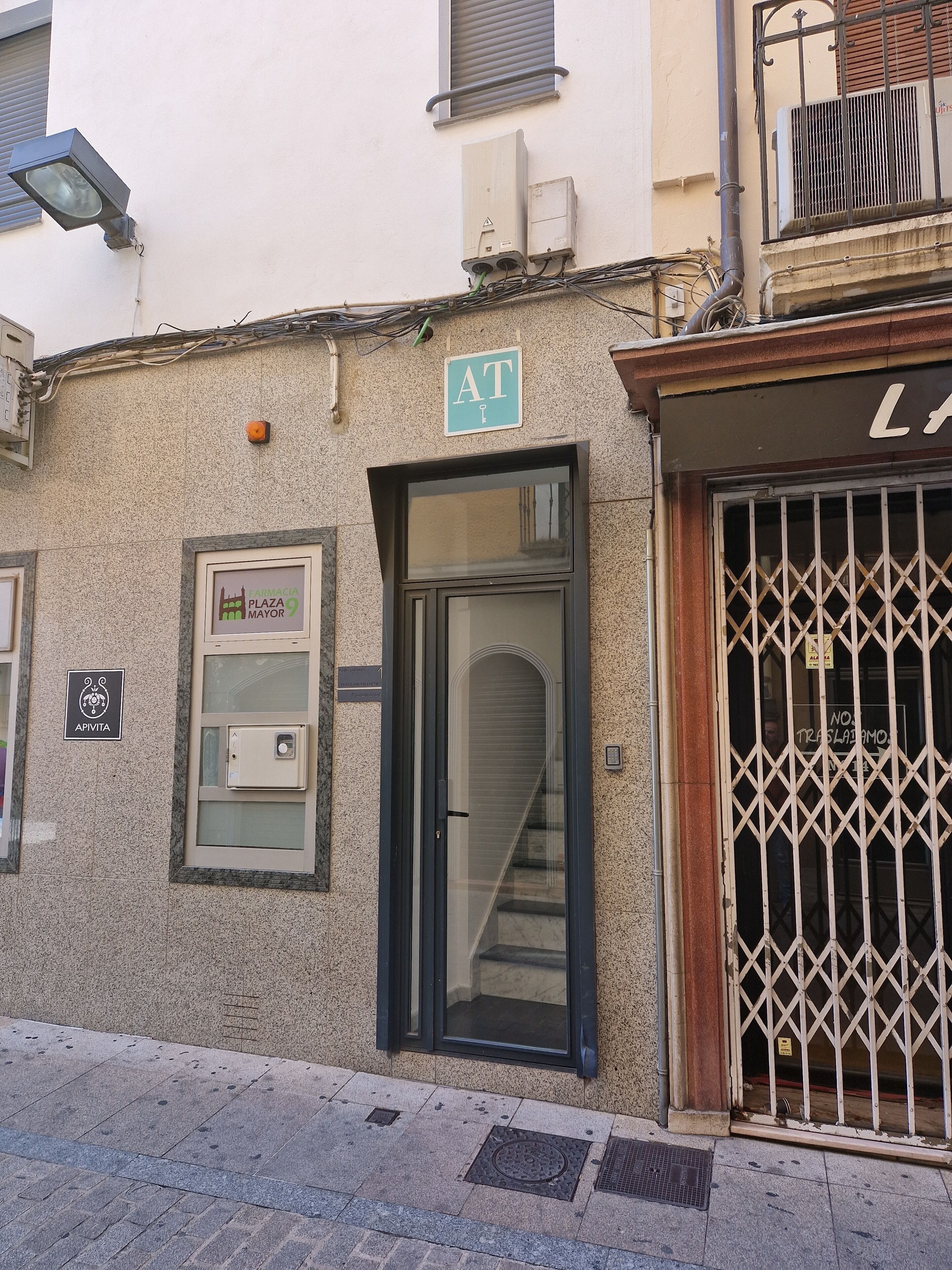 A building facade with a pharmacy sign, a security camera, and a barred entrance.