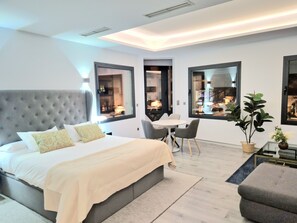 Une chambre moderne avec un grand lit, une table à manger et des chaises. De grandes fenêtres offrent une vue sur la ville.