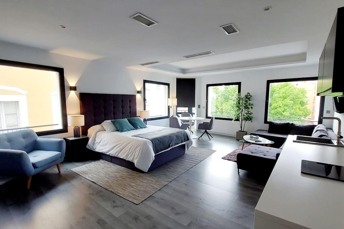 Ein modernes Hotelzimmer mit einem großen Bett, einer Sitzecke mit Tisch und einer Küchenzeile.