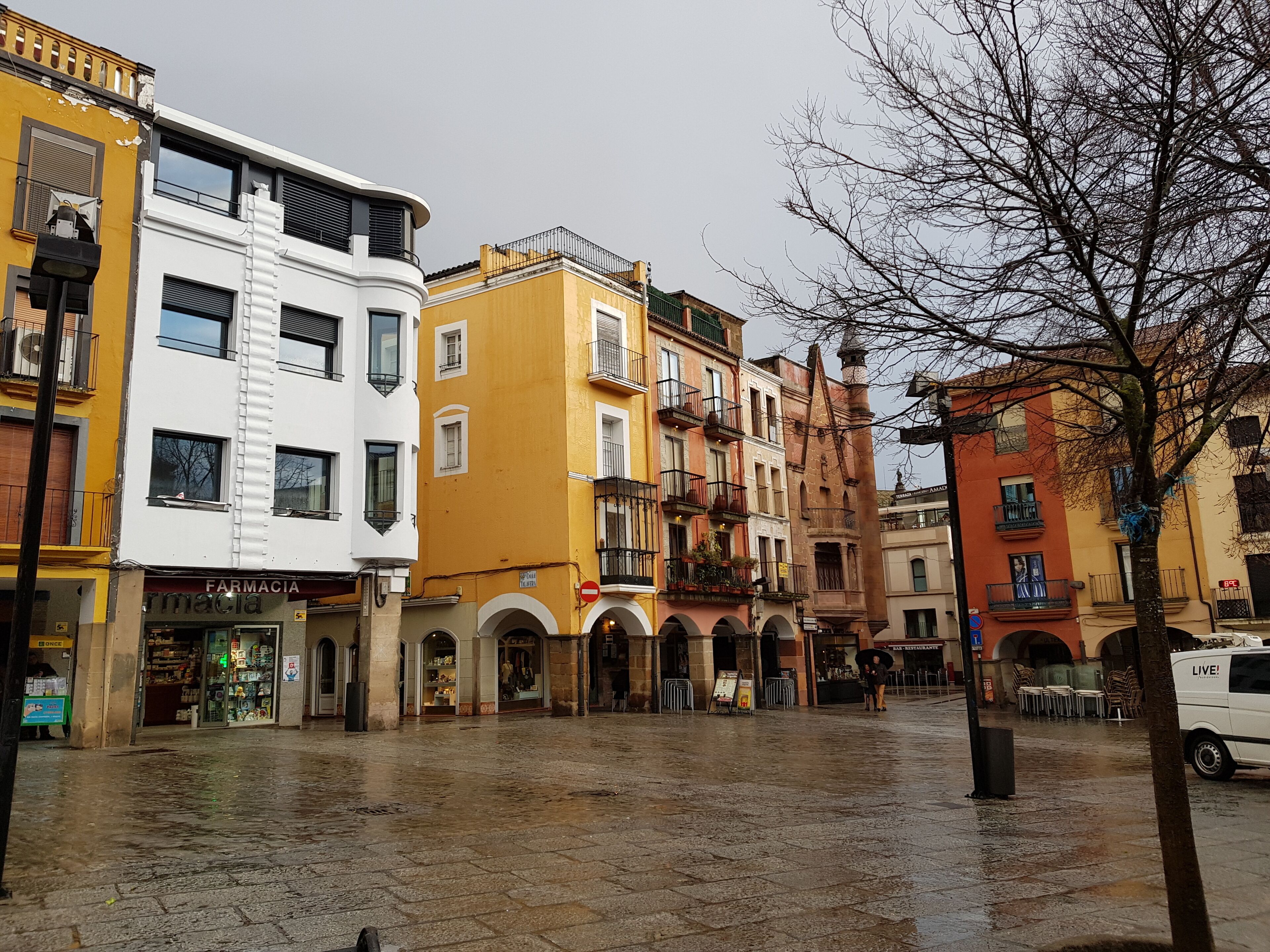 A wet plaza with historic buildings, a pharmacy, and a restaurant.
