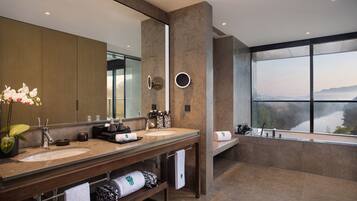 A modern bathroom with dual sinks, a large mirror, and a bathtub with a view of a lake.