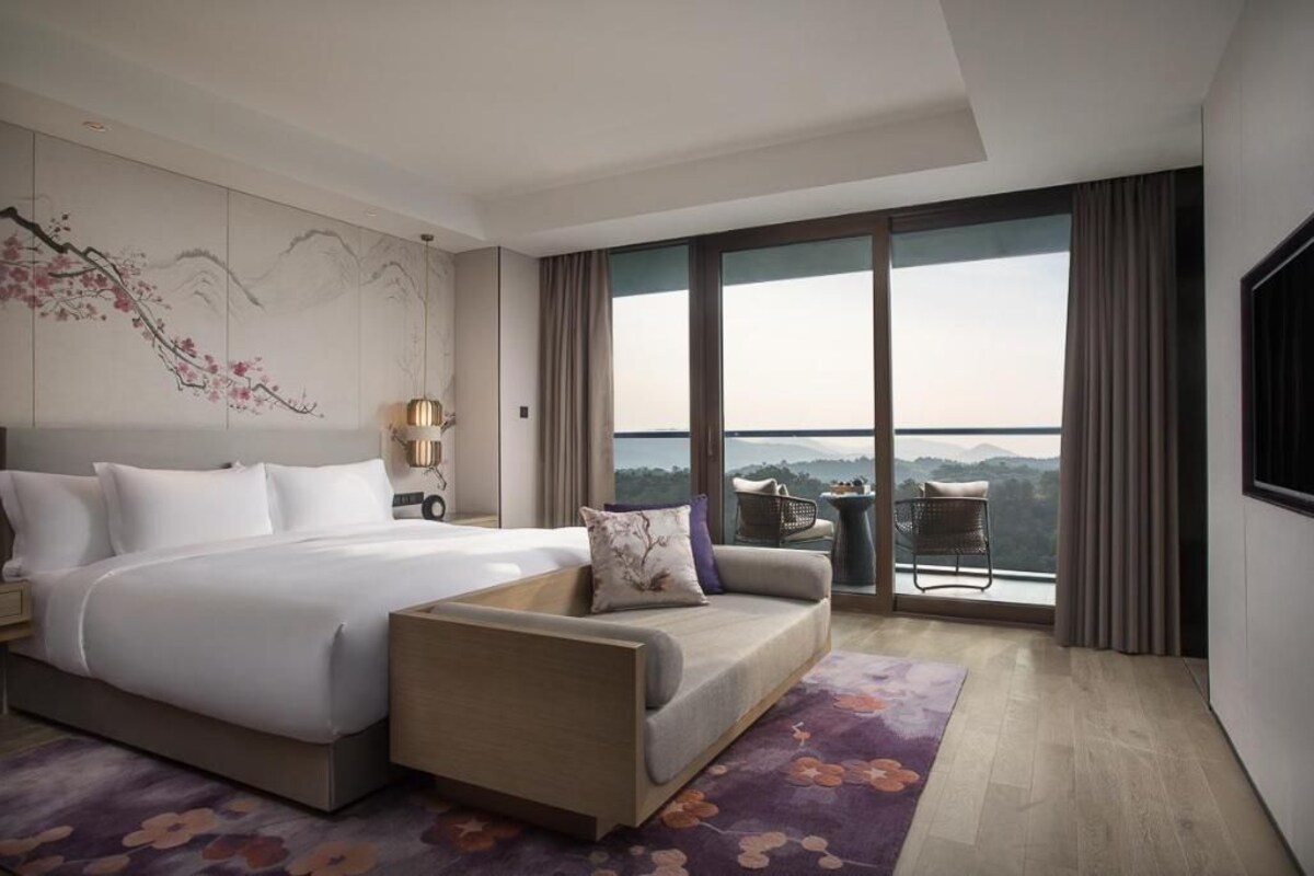 Habitación de hotel con una cama grande, un sofá, vistas a las montañas y un balcón con mesa y sillas.