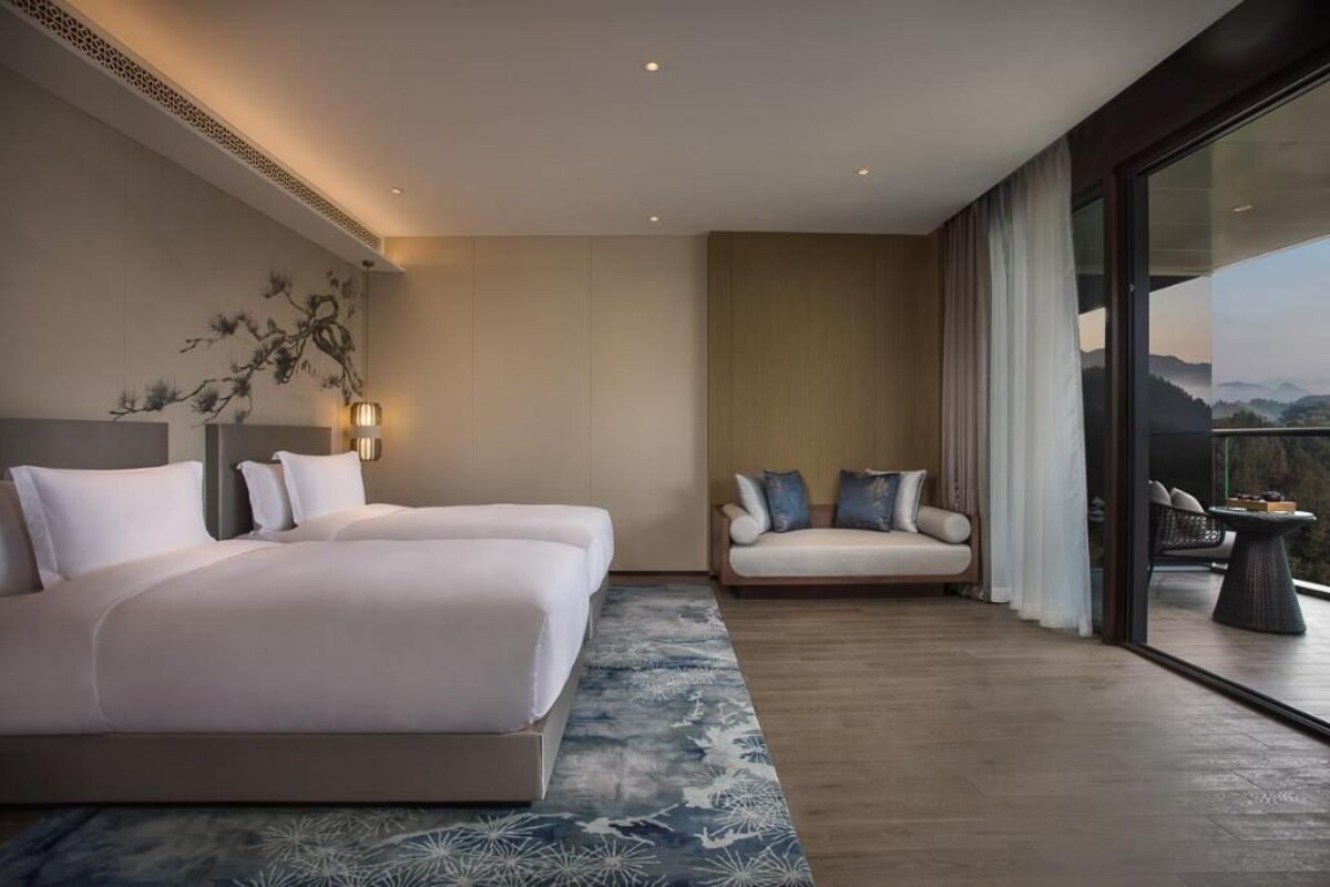 Habitación de hotel moderna con una cama grande, un sofá, una mesita y vistas al exterior.