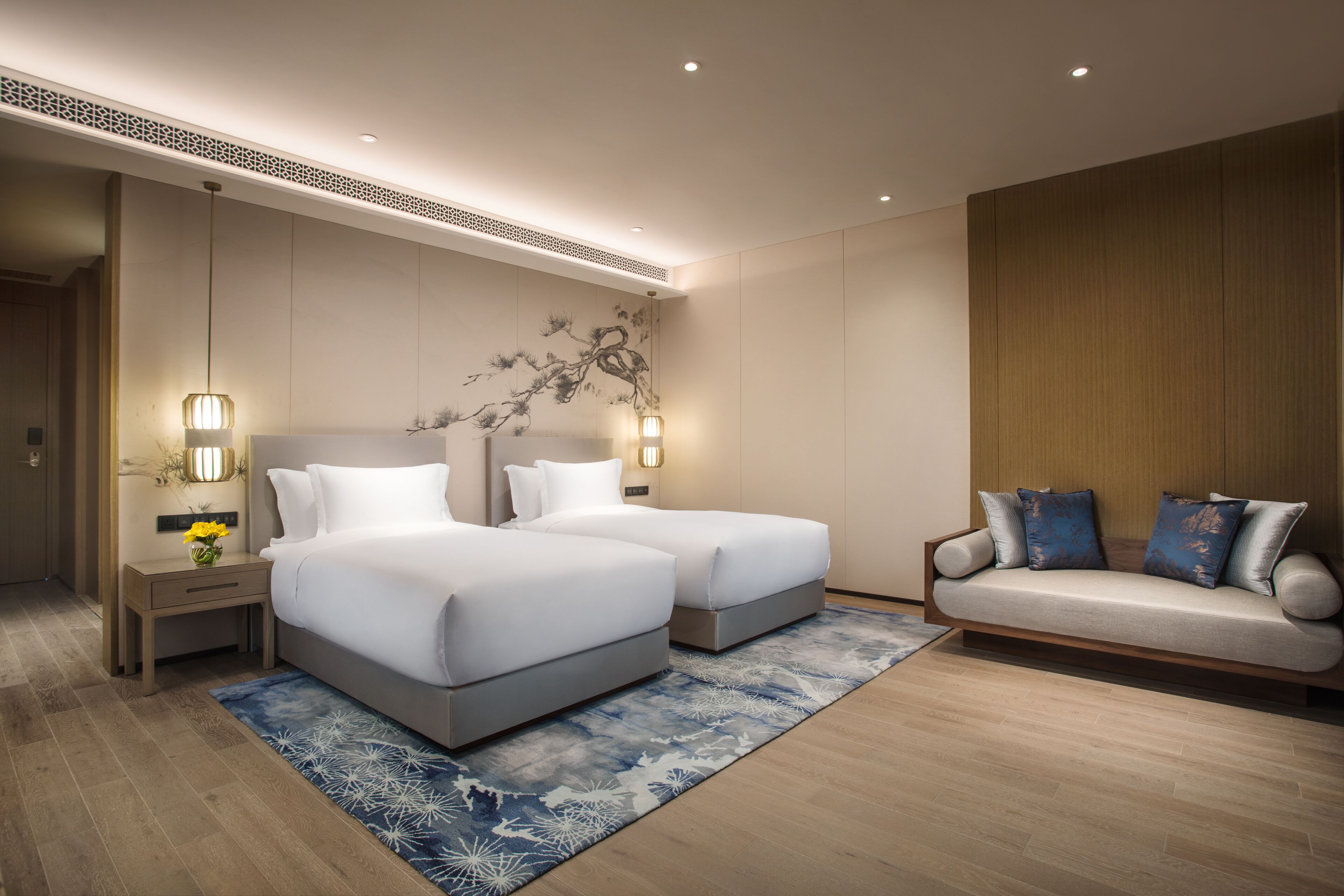 A modern hotel room with two beds, a sofa, and a decorative wall.
