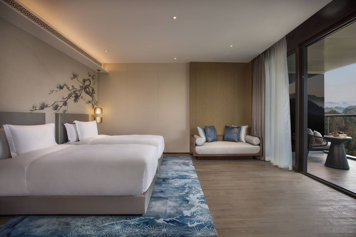 A modern hotel room with a large bed, a sofa, and a balcony with a view.