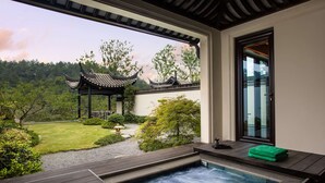A spa area with a hot tub, a wooden deck, and a view of a traditional pavilion in a garden. - Banyan Tree Anji (Huzhou)