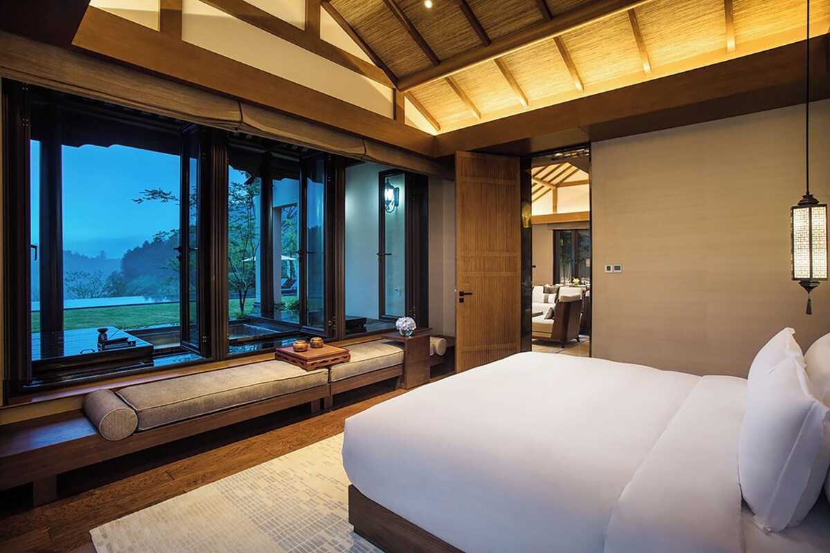 Un dormitorio con una cama grande, una zona de estar con vistas y un techo de madera.