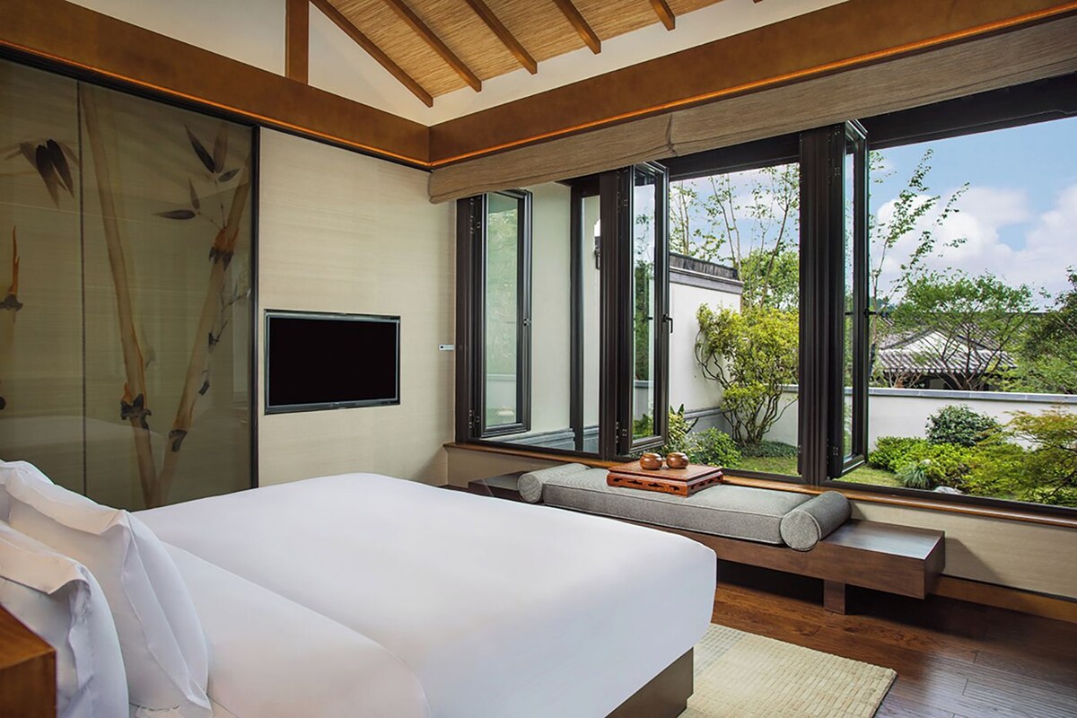 Un dormitorio con cama, televisión y ventanas amplias.