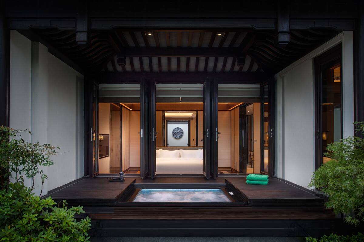 A modern building entrance with a wooden deck, a water feature, and a framed artwork above the door.