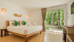 Une chambre spacieuse avec un grand lit, une tête de lit en bois et une vue sur un jardin luxuriant, accessible par une porte-fenêtre coulissante.