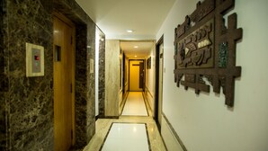Un couloir aux murs de marbre, une porte en bois et un sol carrelé de carreaux blancs.