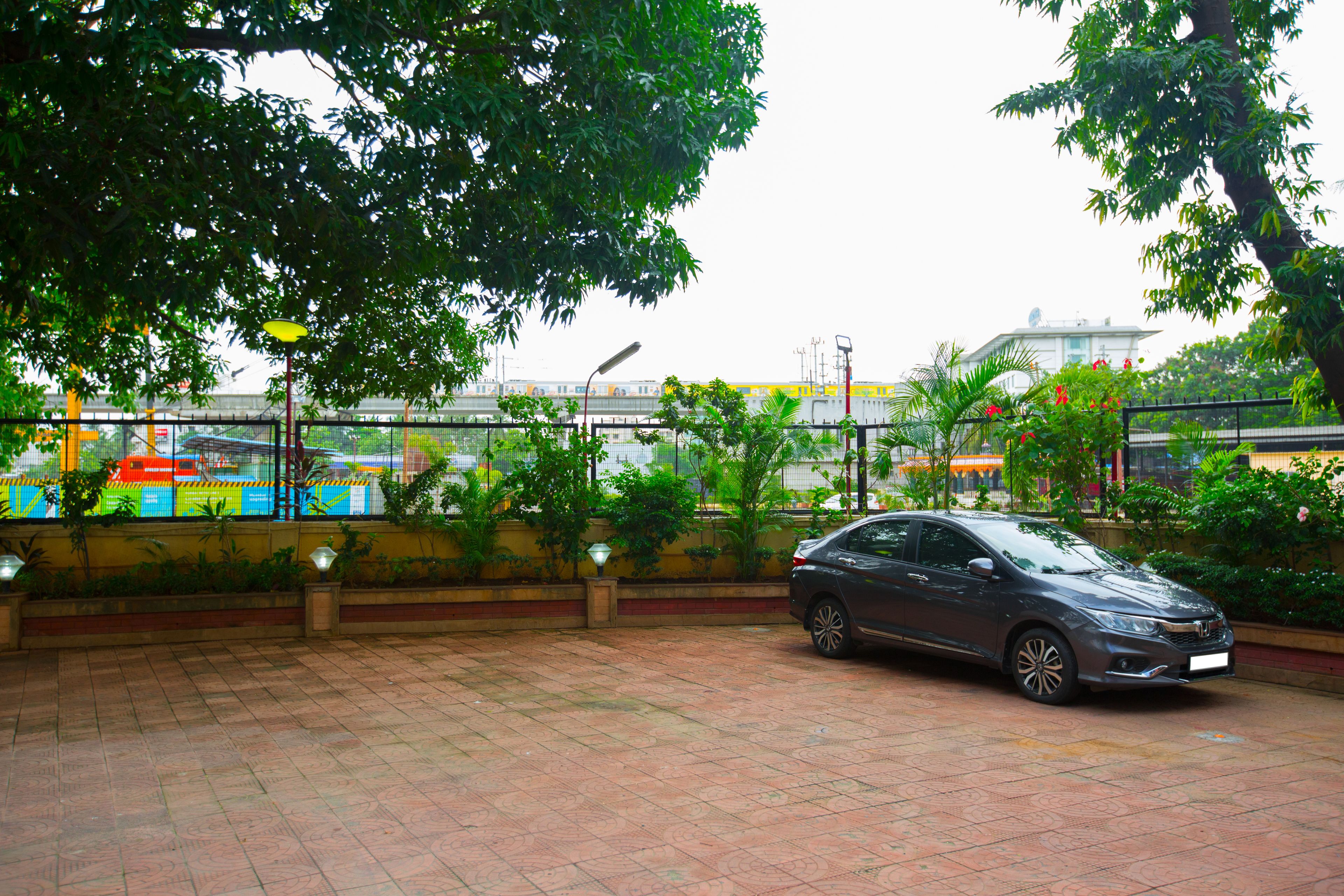 A car parked in a covered outdoor area with tiled flooring, surrounded by greenery and a fence.