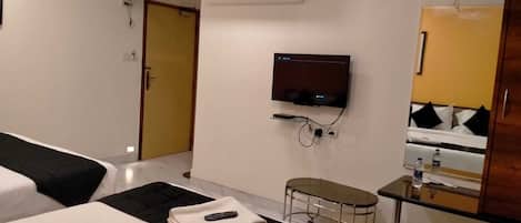 A hotel room with two beds, a TV mounted on the wall, a small table with a chair, and a mirror above the bed.