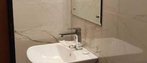 Un baño con pared de mármol, lavamanos blanco, espejo y un cubo de basura.