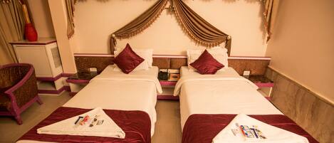 A hotel room with two beds, each with a red bedspread and white pillows. There is a small table between the beds, and a chair to the left.