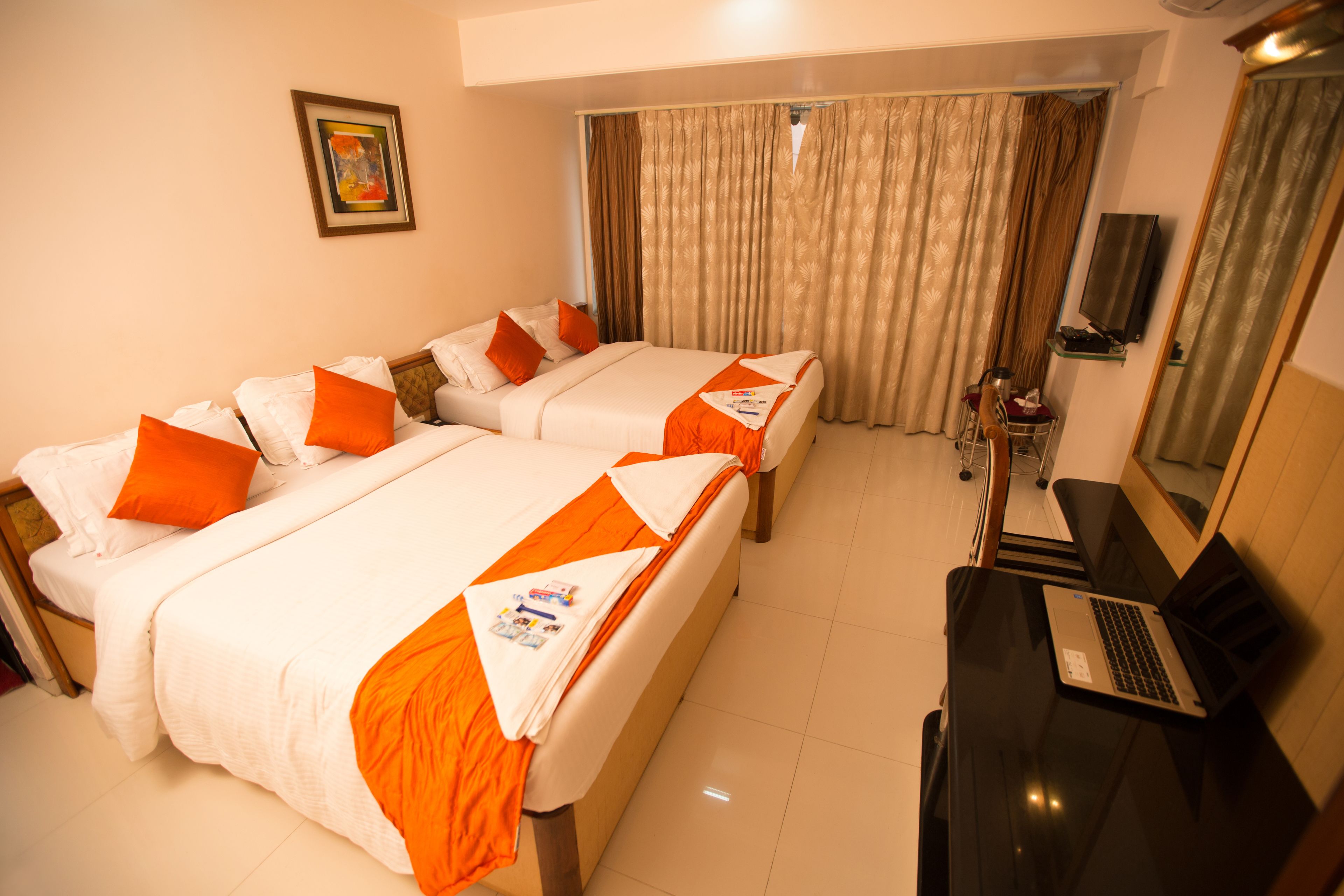 Quarto de hotel com duas camas, uma escrivaninha com um laptop, uma televisão e uma janela com cortinas.