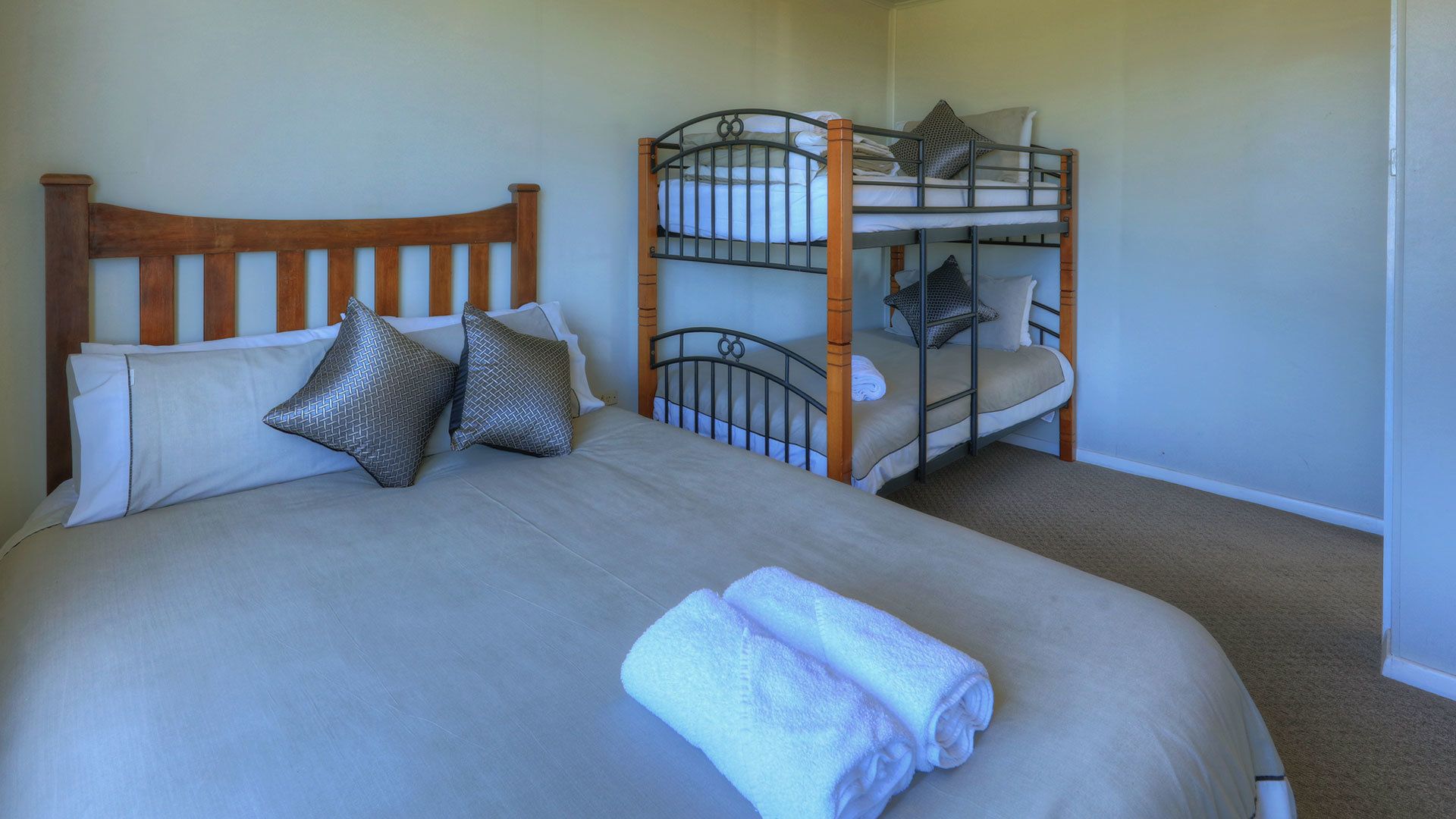 A single bed with a wooden headboard, two pillows, and a rolled towel. A bunk bed is positioned to the right.