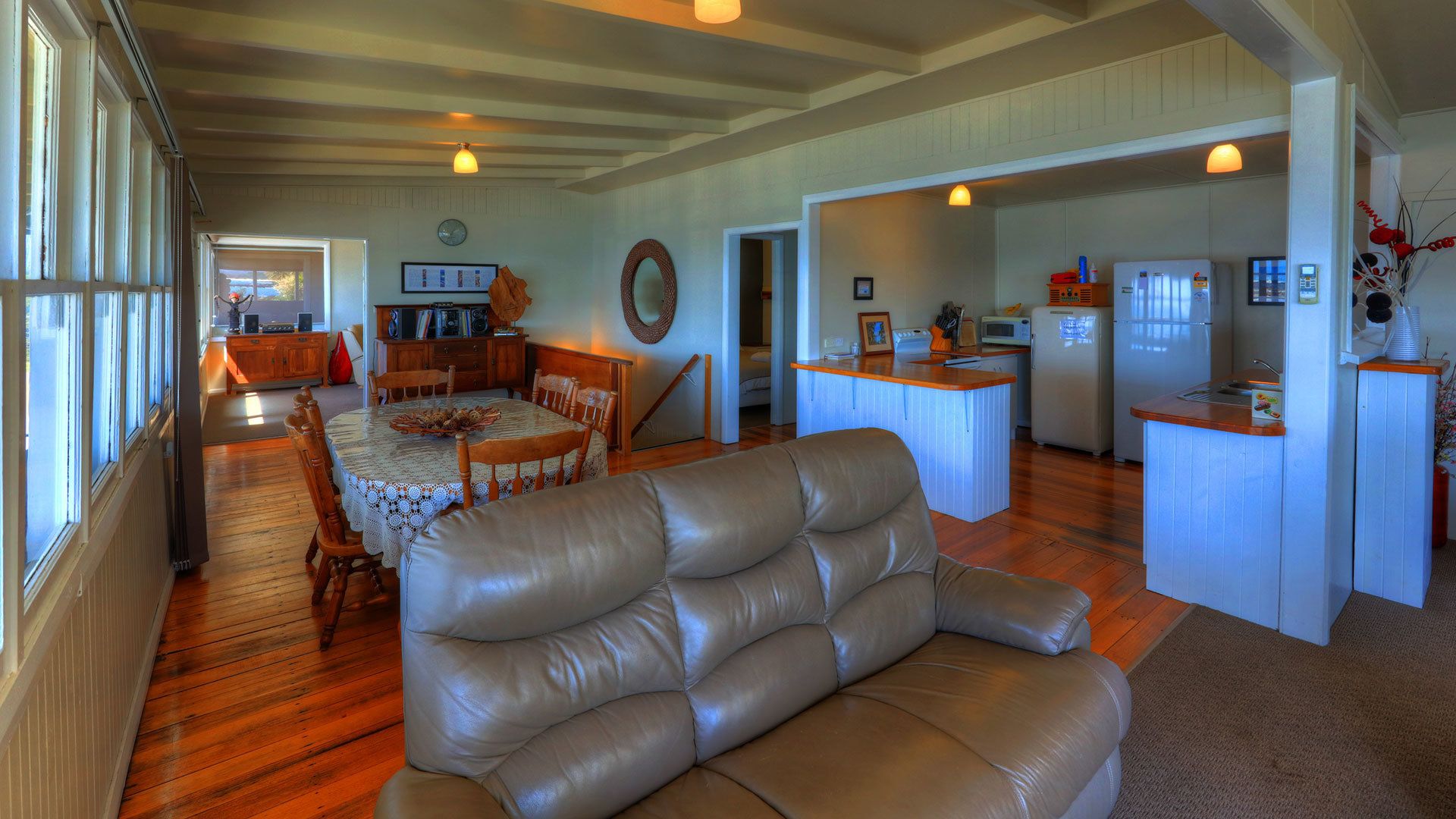 A spacious living room with a leather sofa, wooden dining table, and a kitchen area with a refrigerator and microwave.
