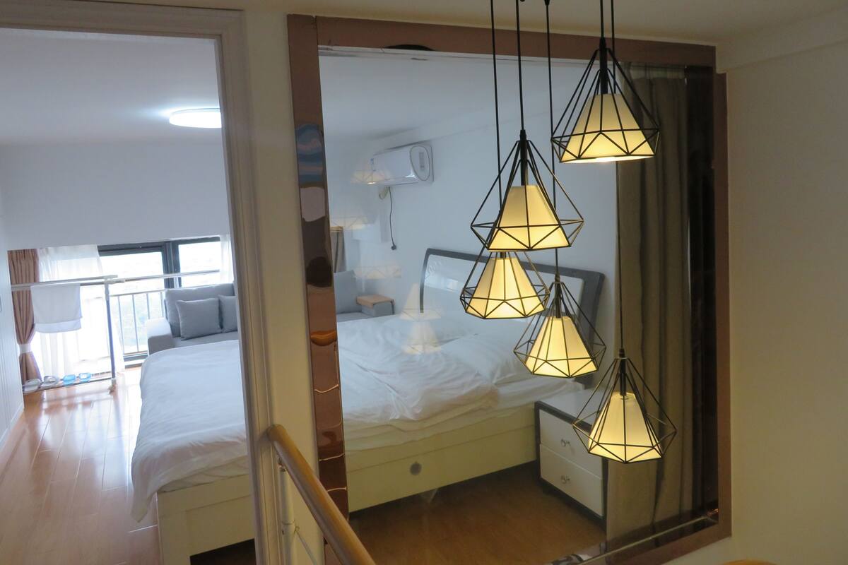 A hotel room with a bed, bedside tables, a mirror, and a hanging light fixture.