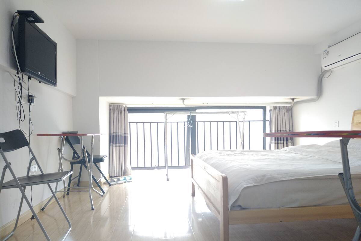 A hotel room with a bed, a desk, a chair, a TV, and a balcony with a view.