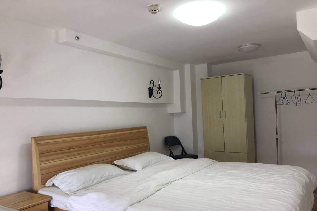 A bedroom with a wooden bed, white bedding, a wardrobe, and a chair.