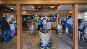A bar area with wooden barrel stools and a stone floor, featuring a variety of bottles and a sign that reads "SIRROMET LIFE STYLE WINE". - Sanctuary By Sirromet (Mount Cotton)