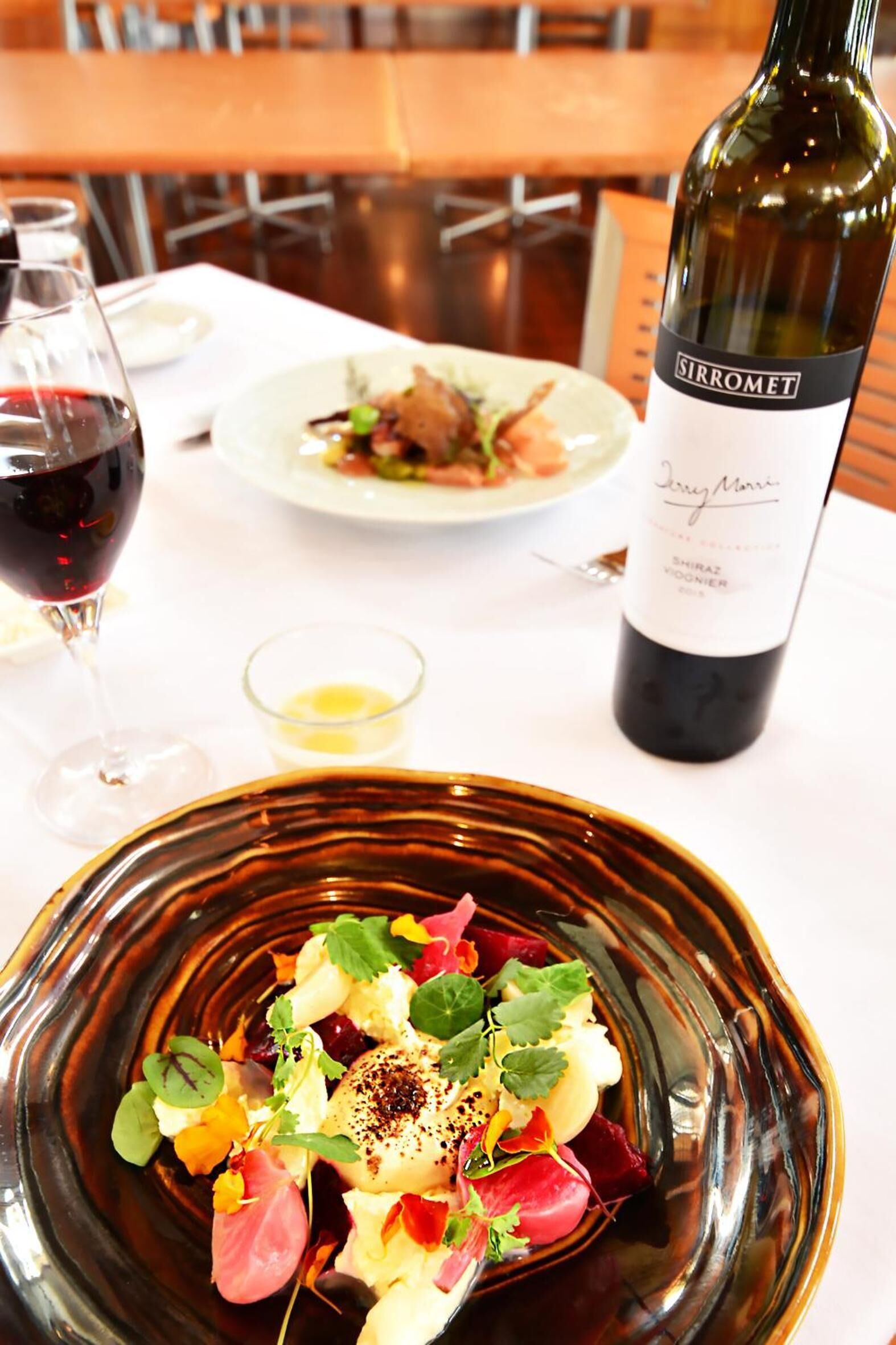 A dining table with a wine bottle, a glass of red wine, and a plate of food.