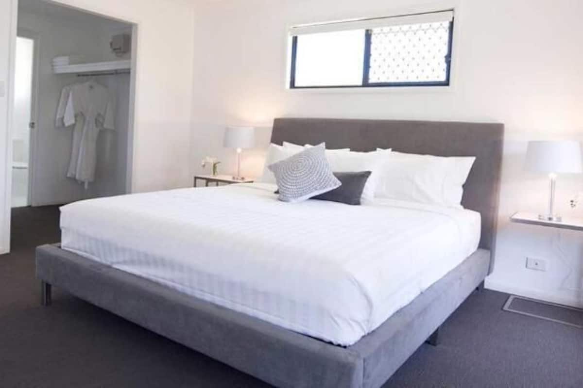 A neatly arranged hotel room with a large bed, bedside tables with lamps, a wardrobe, and a window with blinds.