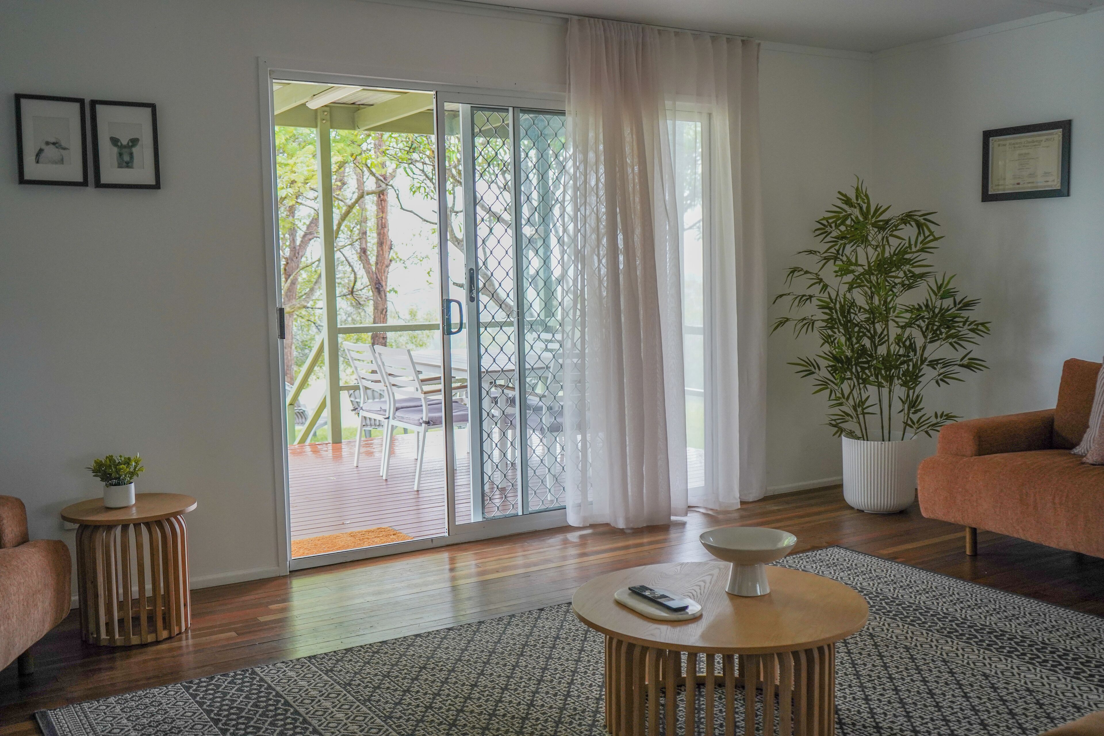 Una sala de estar con una puerta corrediza de vidrio que da a un espacio al aire libre, una planta de bambú en maceta, una mesa redonda de madera y un sofá.