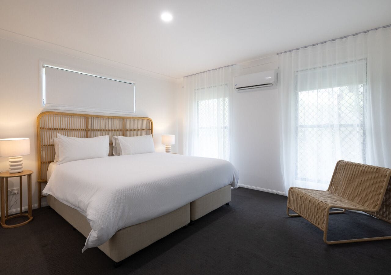 A hotel room with a large bed, a chair, a bedside table, and a window with curtains.