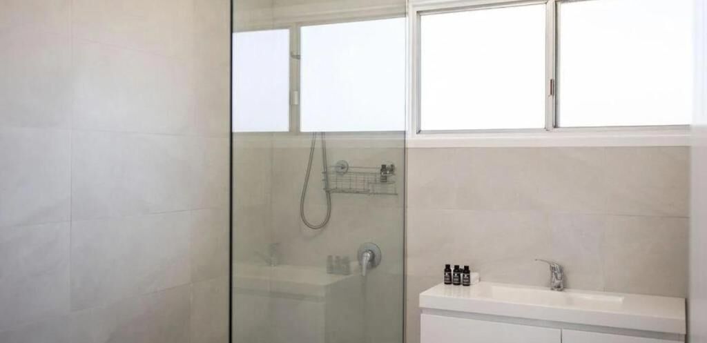 A modern bathroom with a glass-enclosed shower, a white sink, and a window above the sink.