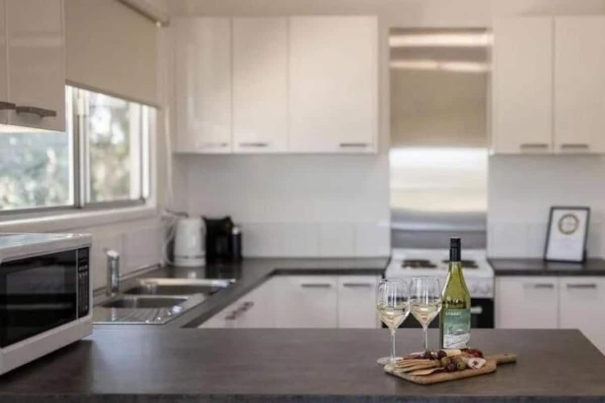 A modern kitchen with white cabinets, a built-in oven, and a central island with two wine glasses and a bottle.