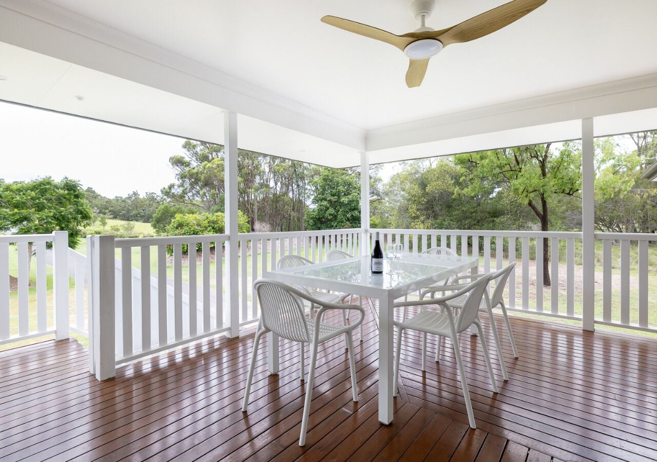 A covered outdoor area with a table and chairs, a ceiling fan, and a view of trees.