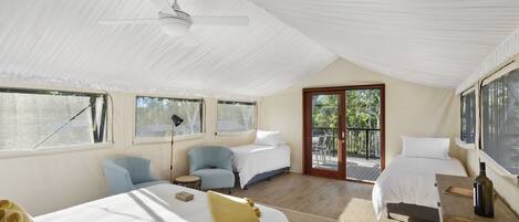 A spacious bedroom with a large bed, two smaller beds, a desk, and a chair. There is a balcony with a view of greenery.