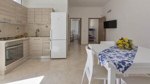 Una cocina moderna con comedor, muebles blancos, un refrigerador y un televisor de pantalla plana en la pared.