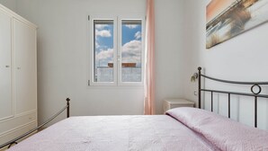 Un dormitorio con cama, armario, ventana con vistas al cielo y un cuadro en la pared.