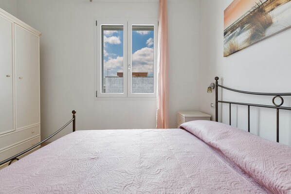 Un dormitorio con cama, armario, ventana con vistas al cielo y un cuadro en la pared.