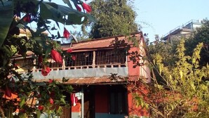 Edifici de dos pisos amb façana vermella i blava, envoltat de verdura i arbres.