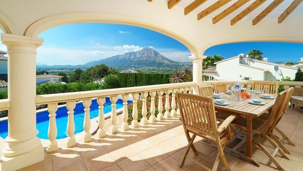 An outdoor patio with a wooden table and chairs, a pool, and a view of a mountain. - Casa Rio - Javea, Costa Blanca (Javea)