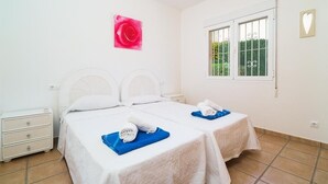 A hotel room with two beds, a window with bars, a white nightstand, and a pink flower decoration. - Casa Rio - Javea, Costa Blanca (Javea)