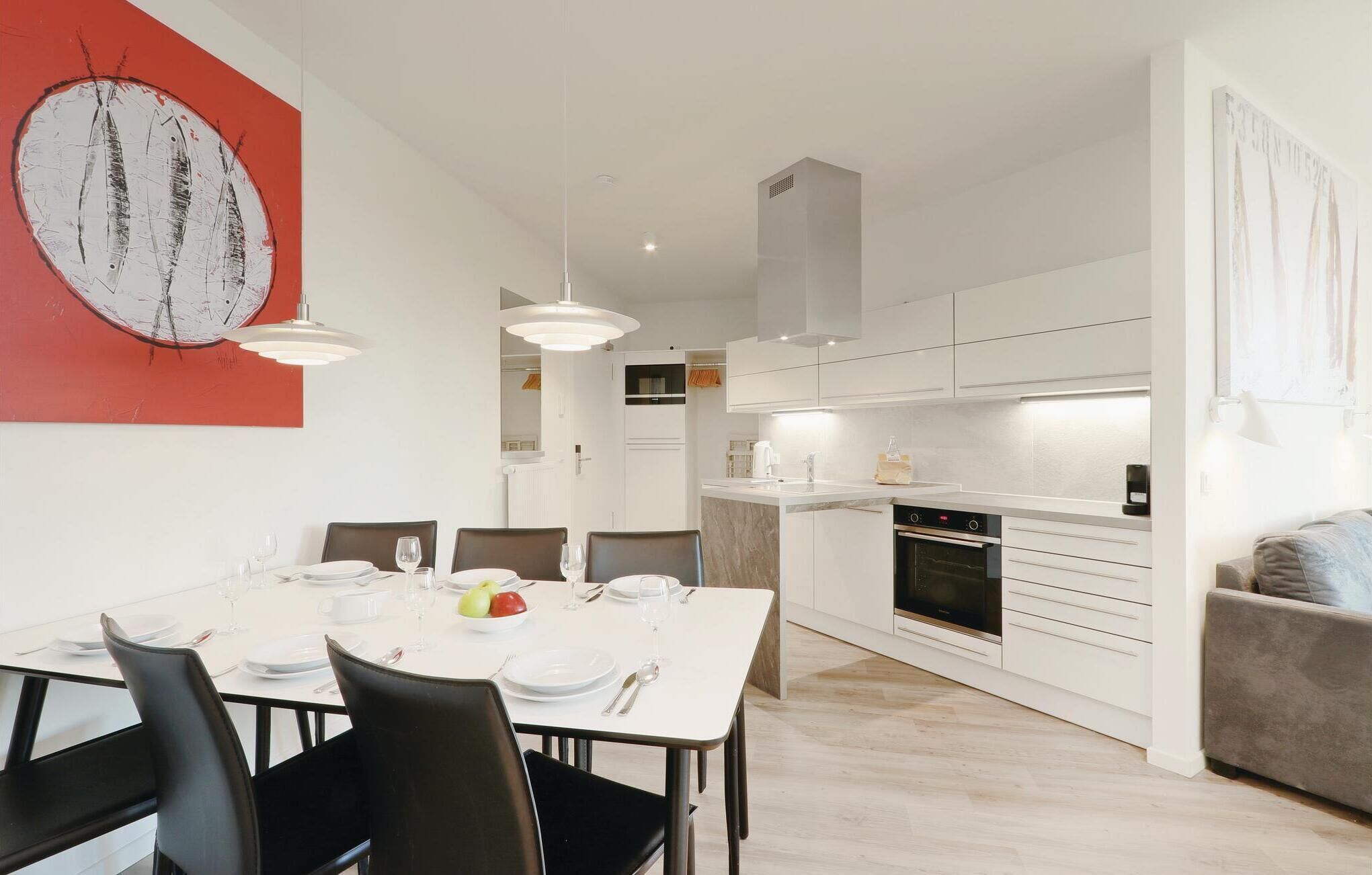 Une cuisine moderne avec des armoires blanches, un four encastré et un coin repas comprenant une table et des chaises blanches.